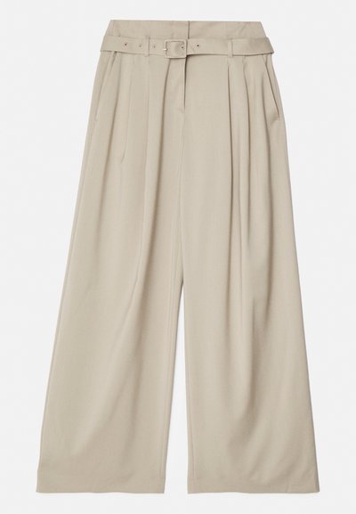 Plati kāju bikses gaiši bežā audumā. Iekļauj augstu jostasvietu, priekšējos krokas un atbilstošu jostu ar metāla sprādzi.