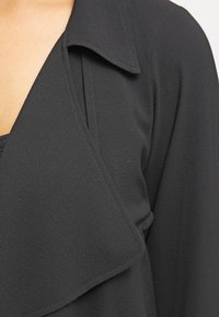 Black blouse featuring a soft, textured fabric, a notch collar, and a draped design with layered front details.