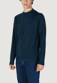 Maglione blu navy in fine maglia con scollo rotondo, maniche lunghe e orlo a costine. Indossato su pantaloni in denim blu.