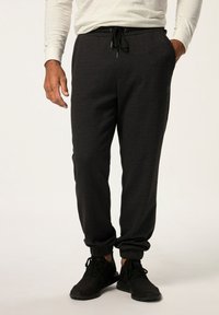 Svarta atletiska joggers med elastisk midja och snörning, avsmalnande vid anklarna. Bärs med svarta sneakers mot en neutral bakgrund.