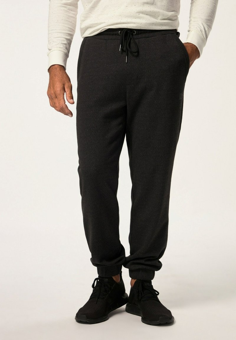 Svarta atletiska joggers med elastisk midja och snörning, avsmalnande vid anklarna. Bärs med svarta sneakers mot en neutral bakgrund.