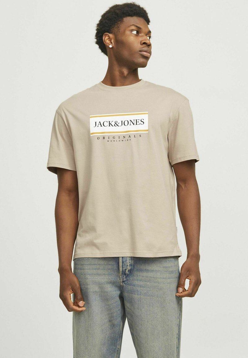 Beige Baumwoll-T-Shirt mit Rundhalsausschnitt und kurzen Ärmeln, das auf der Vorderseite ein grafisches Logo-Design in Schwarz und Gelb aufweist.
