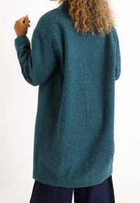 Chaqueta de forro polar en color aqua con un acabado texturizado y acogedor; presenta un corte holgado, bolsillos laterales y un dobladillo ligeramente curvado.