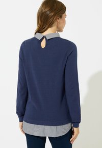 Granatowy sweter z długimi rękawami, z kołnierzykiem i paskowanym wykończeniem w dolnej części, oraz detalem w formie otworu na plecach. Miękki materiał o gładkiej fakturze.