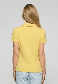 Żółta koszulka polo z klasycznym kołnierzykiem, krótkimi rękawami i gładką fakturą, w zestawieniu z jasnoniebieskimi dżinsami.