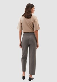 Top beige recortado con mangas cortas combinado con pantalones gris de cintura alta. Los pantalones presentan una sutil textura de rayas verticales y un diseño elegante.