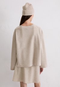 Be�żowy zestaw swetra i spódnicy wykonany z miękkiego, teksturowanego materiału. Sweter ma szeroki dekolt i luźny krój, podczas gdy spódnica ma rozszerzany fason.