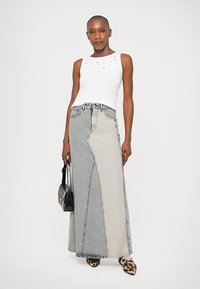 Fehér, ujjatlan felső díszítéssel, hosszú, aszimmetrikus, világos és sötétkék árnyalatú farmer szoknyával párosítva. Zsákmány mintás cipők.