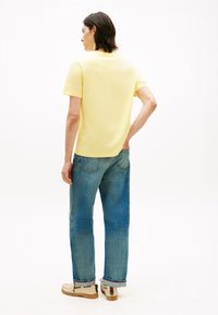 Yellow cotton t-shirt with a crew neck, paired with blue denim jeans. Visible stitching on the jeans and light-colored footwear.