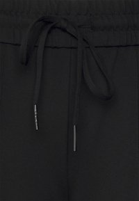 Black sweatpants feature a textured, elastic waistband with a drawstring closure and metal aglets. The fabric is smooth and breathable.