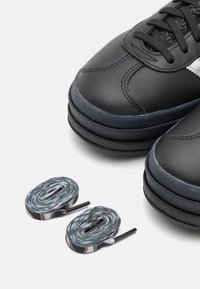 Svarta lädersneakers med texturerad ovandel, lager på lager svart gummisula och två flerfärgat mönstrade snören med svarta spetsar.