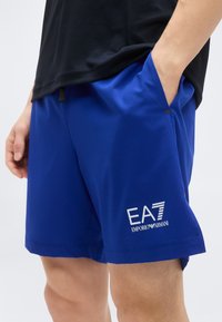 Μπλε αθλητικό σορτς από ελαφρύ ύφασμα, με πλαϊνές τσέπες και λογότυπο "EA7 Emporio Armani" σε λευκό χρώμα.
