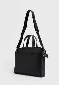 Μαύρη λεπτή τσάντα χειρός με διπλές λαβές στο πάνω μέρος και ρυθμιζόμενο ιμάντα ώμου, απεικονίζεται σε απλό φωτεινό φόντο.