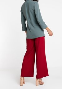 Šedé tričko s třičtvrtečními rukávy a široké červené kalhoty bez vzoru s hladkým povrchem. Hnědé vysoké podpatky.