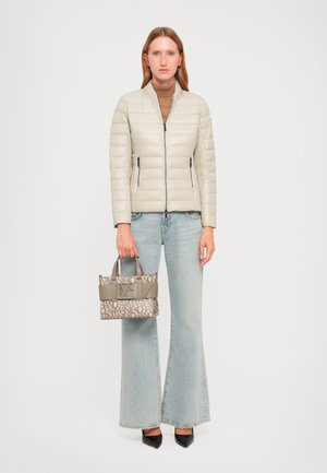 Woman wearing a light beige quilted jacket, brown turtleneck, light blue flared jeans, black pointed shoes, holding a beige patterned handbag.