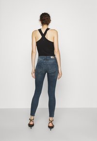 Top de tirantes negro acanalado con diseño de espalda cruzada, combinado con vaqueros skinny azul oscuro con dobladillo deshilachado y bolsillos traseros.