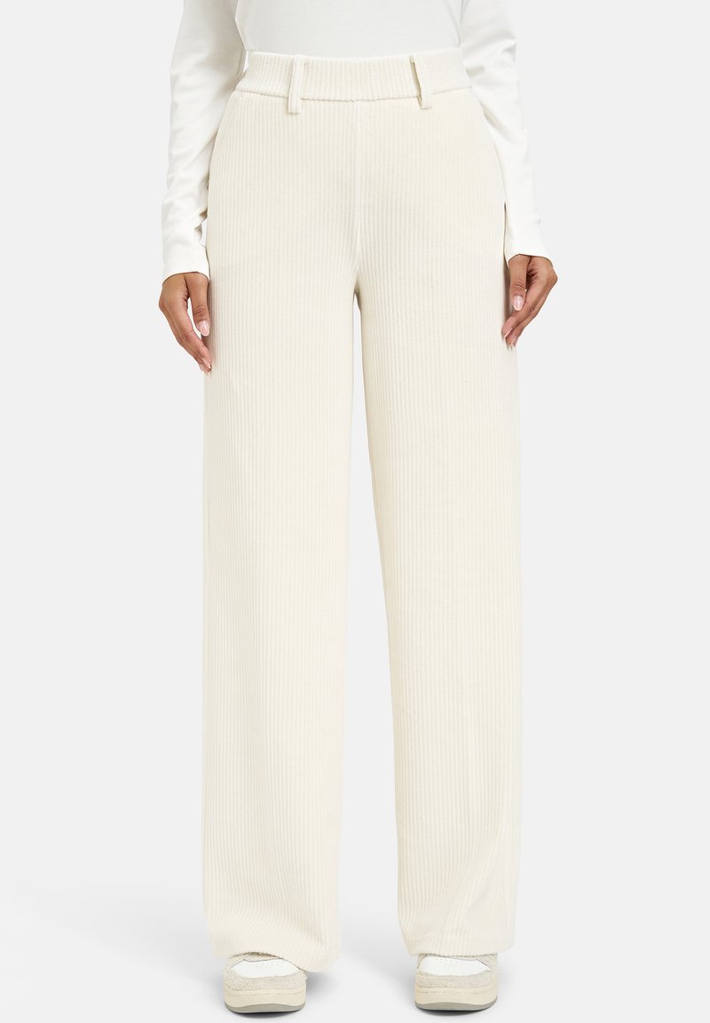 Cream ribbed wide-leg trousers featuring a high waist and belt loops, with a soft texture and pleat details, paired with white sneakers.