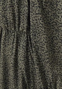 Tissu vert olive avec un motif imprimé animal noir, présentant des coutures froncées le long d'une section pour ajouter texture et dimension.