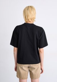 T-shirt nera in cotone con maniche corte, scollo a girocollo e vestibilità rilassata, abbinata a pantaloni beige con un tessuto testurizzato e tasche sul retro.