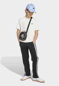 T-shirt blanc à col rond avec logo noir, joggers noirs avec bandes latérales blanches, casquette bleu clair et sac bandoulière noir rond avec logo.