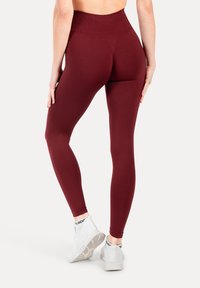 Bordowe legginsy z wysokim stanem z teksturowanym wzorem po bokach, w połączeniu z białymi butami sportowymi.