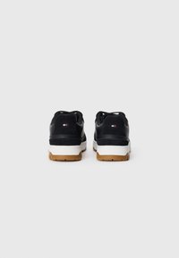 Black sneakers with suede and synthetic materials, white midsole, and rubber outsole. Features minimal branding on the heel.