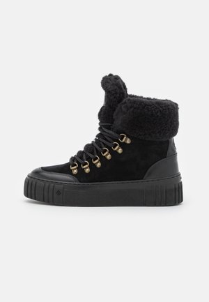 Black suede ankle boots with a fluffy black cuff, gold eyelets, and black laces. The sole is textured and platform-style.