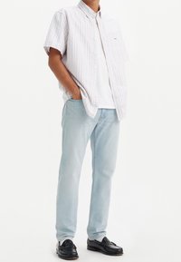 Camisa de manga corta a rayas en colores pastel, combinada con una camiseta blanca, vaqueros de color azul claro y mocasines negros.