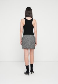 Zwarte mouwloze top gecombineerd met een gestructureerde grijze minirok met franjes aan de onderkant. Zwarte sokken en puntige hakken maken de outfit compleet.