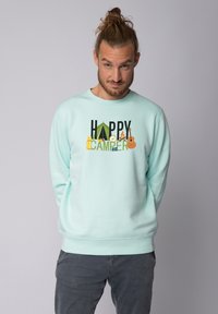 Sweatshirt turquoise clair avec graphique "HAPPY CAMPER" et éléments de camping. Manches et ourlet côtelés, col rond, texture douce.