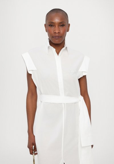 White shirt dress with a collar, capped sleeves, and a tied belt. Made of lightweight fabric, featuring a button-down front and subtle embroidery.