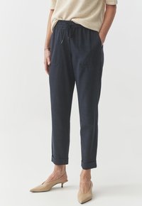 Navy blue, elastic-waist pants with two front pockets, cuffed hems, and a lightweight texture, paired with light beige pointy-toed heels.