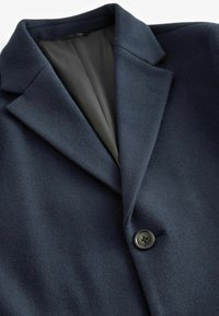 Abrigo de lana azul marino oscuro con cuello con muesca, cierre de un solo botón y un forro negro suave, que muestra una textura suave y un ajuste a medida.