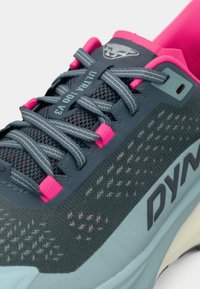 Γκρι αθλητικό παπούτσι με επάνω μέρος από πλέγμα και ροζ λεπτομέρειες, ενισχυμένη μύτη και μαλακή σόλα. Ορατή η ετικέτα "Ultra 100 V3" στη γλώσσα.