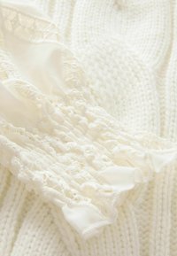 Bílá pletená svetr fabric s texturovaným vzorem, s detaily na rukávech v podobě zřaseného provedení a krajkového lemu, vše v odpovídajícím měkkém odstínu.