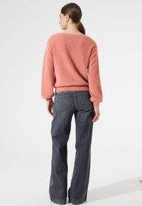 Flauschiger, rosa Pullover mit weit geschnittenem Halsausschnitt und Ballonärmeln, kombiniert mit hochtaillierten, dunklen Jeans mit Gesäßtaschen.