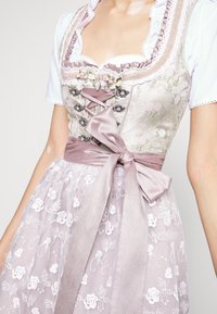 Tradycyjna sukienka z kwiecistą górą w jasnych odcieniach, ozdobiona koronką, wstążką i przezroczystą, haftowaną spódnicą.
