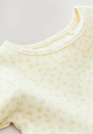 Ljusgul långärmad topp i ribbat tyg, prydd med små blommönster i rosa och grönt. Rundad halsringning och mjuk textur.