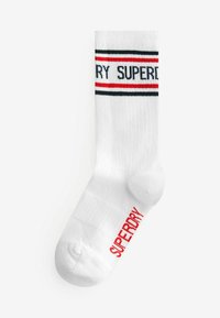Valge ribaga lühikesed sokid punaste ja mustade triipudega, millel on punane "SUPERDRY" tekst jalas ja osaliselt nähtav must tekst säärel.