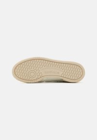 Sole sneakers značky Reebok v světle béžové barvě, texturovaný povrch, kruhový emblém a vzor s diamantovými výstupky pro trakci.