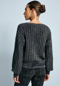 Mørk grå, ribbet sweater med en afslappet pasform og ballonærmer. Blød tekstur, med en kant der sidder ved taljen.