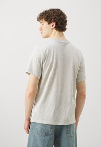 Gray cotton t-shirt with short sleeves, crew neck, and a relaxed fit. Fabric has a smooth texture. Worn with light blue denim jeans.