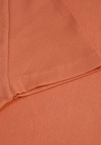 Tejido de algodón acanalado en un suave color durazno, que muestra una textura lisa y costuras bien terminadas con un brillo sutil.