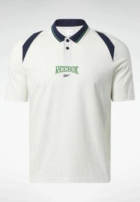 Polo blanc Reebok avec accents de col bleu marine et vert, panneaux d'épaule bleu marine, portant un logo Reebok vert brodé sur la poitrine.