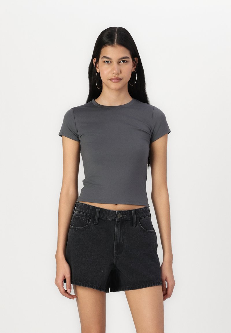 Sivý crop top s krátkym rukávom vyrobený z elastického materiálu, skombinovaný s čiernymi denims krátkymi nohavicami s vysokým pásom, ktoré majú rozstrapkaný lem a vreck�á.