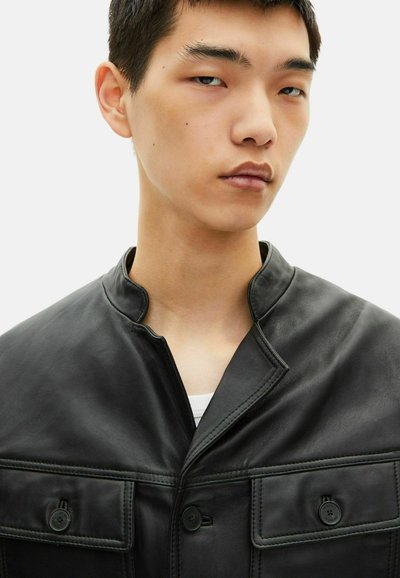 Chaqueta de cuero negra con un cuello alto, cierre de botones en el frente y dos bolsillos en el pecho con costuras detalladas y botones negros.