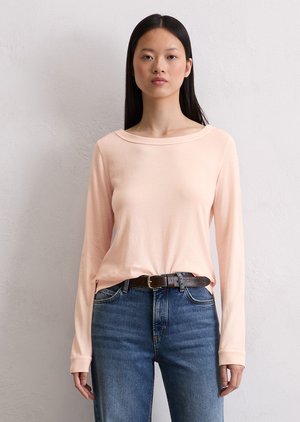 T-shirt à manches longues rose pâle avec un col bateau, fabriqué en tissu doux ; associé à un jean bleu taille haute légèrement déchiré et une ceinture marron.