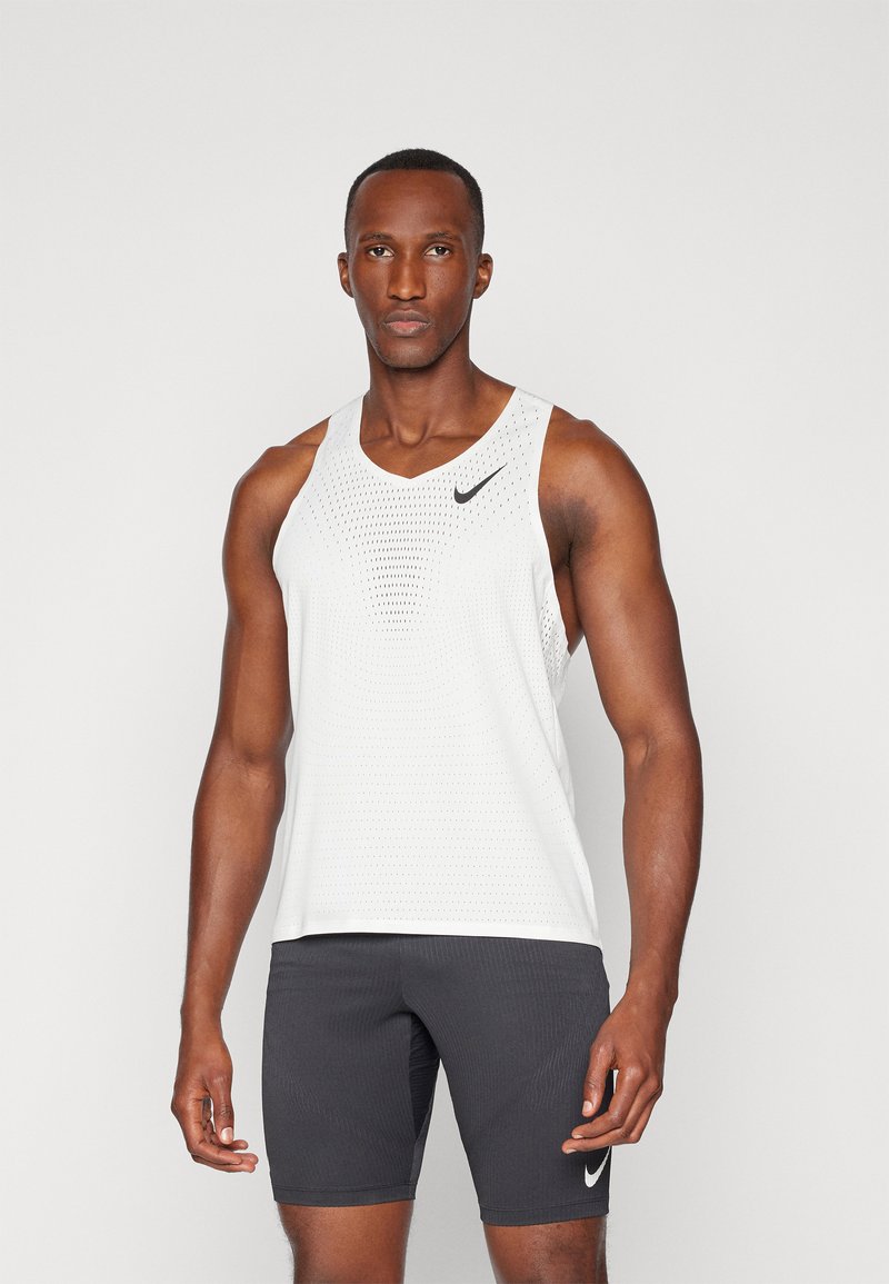 Weißes ärmelloses Sport-Tanktop mit Netzdesign und schwarzem Nike-Logo, kombiniert mit schwarzen enganliegenden Shorts mit weißem Logo.