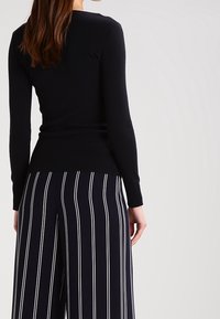 Musta pitkähihainen neule ribbineuloksella, yhdistetty tummansinisiin ja valkoisiin pystysuoraan raidoitettuihin leveälahkeisiin housuihin.