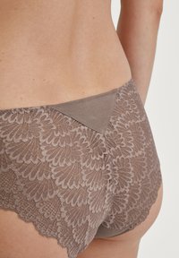 Bruine hoge slip met kant, voorzien van een bloemenpatroon en een gladde effen tailleband. De textuur is delicaat met golvende randen.